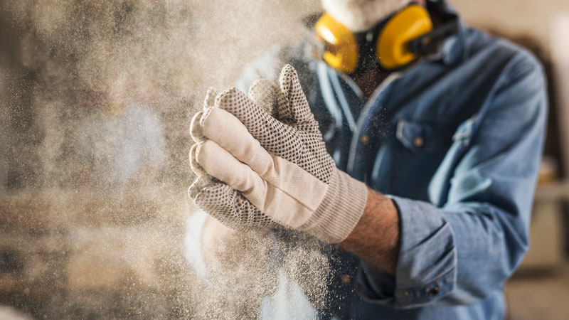 Carpenter cleaning work gloves from sawdust after he finished processing the wood